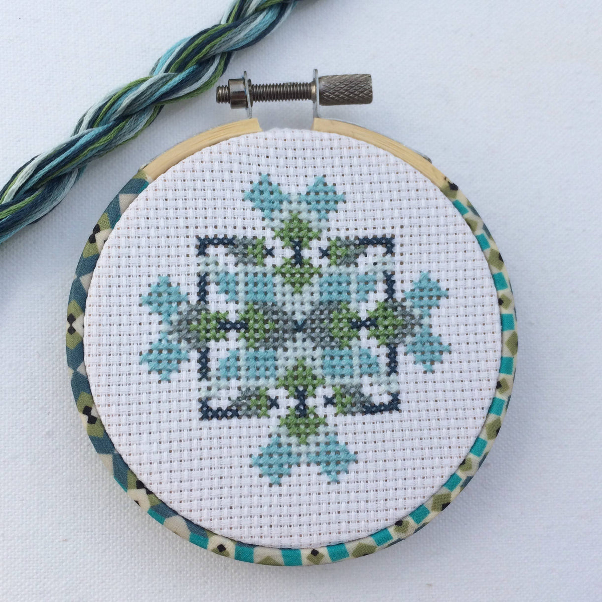 The finished mini geometric hoop with matching blue and green thread