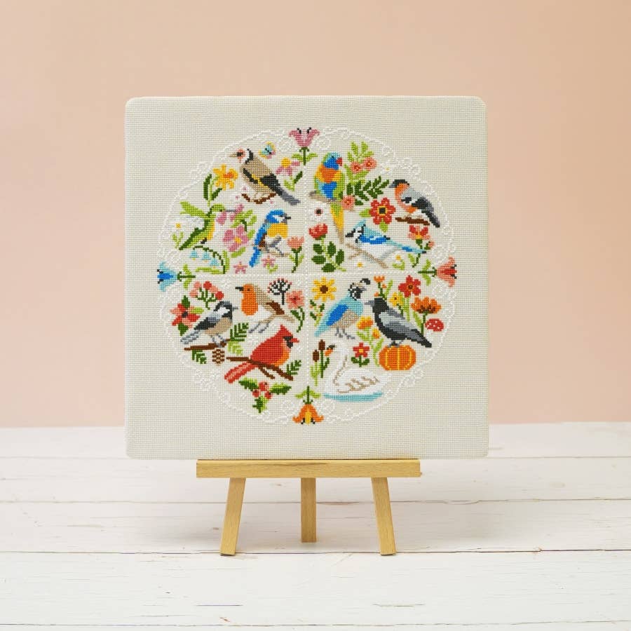 Song of the Seasons cross stitch design featuring birds from four continents on sand colored 14 count aida